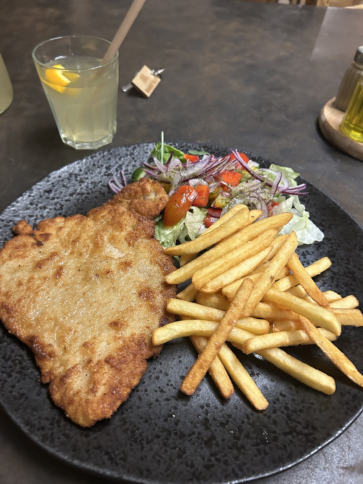 Kotlet panierowany z frytkami i surówką na czarnym talerzu